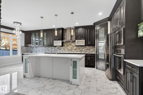 Kitchen featuring glass insert cabinets, light marble finish flooring, stainless steel appliances, decorative light fixtures, and ornamental molding - 8536 19 Avenue, Edmonton, AB - Indoor Photo Showing Kitchen With Upgraded Kitchen