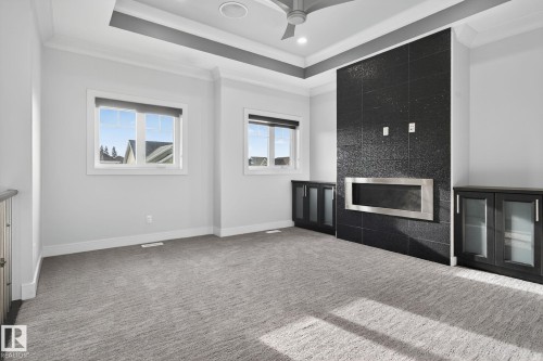 Unfurnished living room with crown molding, a tile fireplace, carpet, a ceiling fan, and a raised ceiling - 8536 19 Avenue, Edmonton, AB - Indoor Photo Showing Other Room