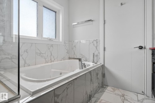 Bathroom with a tub with jets, light marble finish flooring, and tile walls - 8536 19 Avenue, Edmonton, AB - Indoor Photo Showing Bathroom