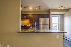 Kitchen featuring tasteful backsplash, stainless steel appliances, a peninsula, under cabinet range hood, and dark stone countertops - 