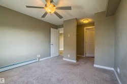 Unfurnished bedroom featuring a textured ceiling, light colored carpet, a ceiling fan, and baseboard heating - 