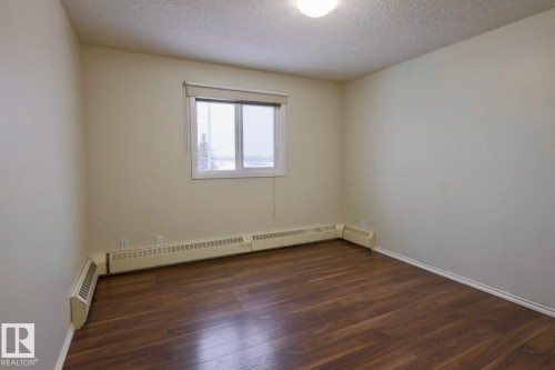 Spare room with dark wood-style floors, a textured ceiling, and a baseboard heating unit - 213 5065 31 Avenue, Edmonton, AB - Indoor Photo Showing Other Room