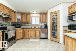 Kitchen with stainless steel appliances, brown cabinets, backsplash, light countertops, and under cabinet range hood - 