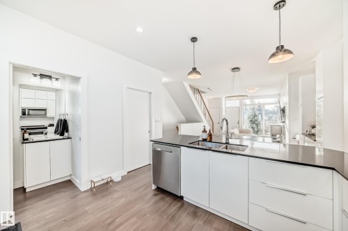 Kitchen with modern cabinets, white cabinets, decorative light fixtures, light wood finished floors, and stainless steel appliances - 14812 98 Avenue, Edmonton, AB - Indoor Photo Showing Kitchen With Upgraded Kitchen