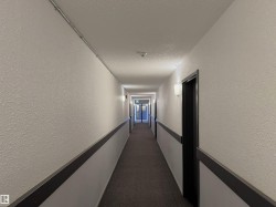 Corridor featuring dark carpet, a textured wall, and a textured ceiling - 