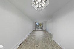 Unfurnished living room featuring light wood-type flooring, a baseboard radiator, and a chandelier - 