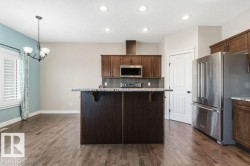 Kitchen featuring appliances with stainless steel finishes, backsplash, a kitchen breakfast bar, light stone counters, and hanging light fixtures - 