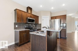 Kitchen with decorative backsplash, appliances with stainless steel finishes, light stone countertops, dark wood-type flooring, and an island with sink - 