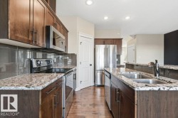 Kitchen with stainless steel appliances, dark wood-style flooring, a textured ceiling, light stone counters, and dark brown cabinets - 