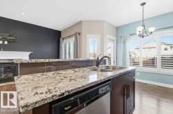 Kitchen with light wood-type flooring, stainless steel dishwasher, pendant lighting, light stone countertops, and dark brown cabinets - 