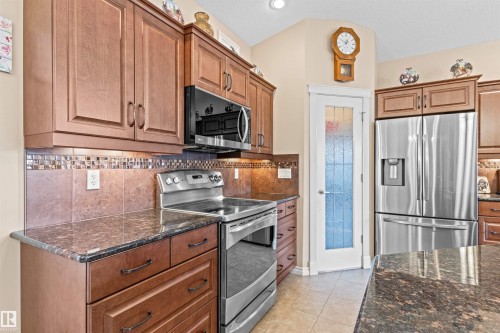 Kitchen with stainless steel appliances, tasteful backsplash, light tile patterned floors, dark stone counters, and vaulted ceiling - 50 Willow Wood Lane, Stony Plain, AB - Indoor Photo Showing Kitchen With Stainless Steel Kitchen