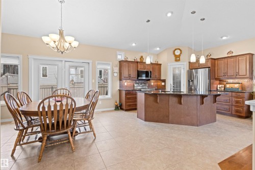 Kitchen with tasteful backsplash, dark stone countertops, a breakfast bar area, brown cabinetry, and a kitchen island with sink - 50 Willow Wood Lane, Stony Plain, AB - Indoor
