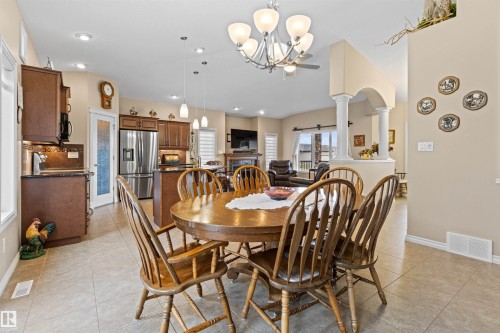 Dining area featuring a glass covered fireplace, light tile patterned floors, a chandelier, arched walkways, and recessed lighting - 50 Willow Wood Lane, Stony Plain, AB - Indoor Photo Showing Dining Room