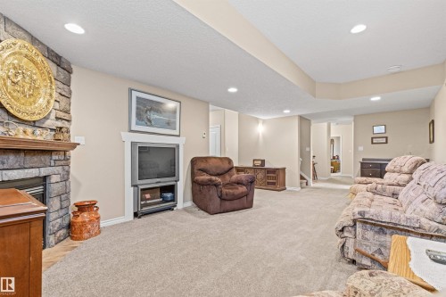 Living room with light carpet, recessed lighting, a stone fireplace, a textured ceiling, and stairway - 50 Willow Wood Lane, Stony Plain, AB - Indoor With Fireplace