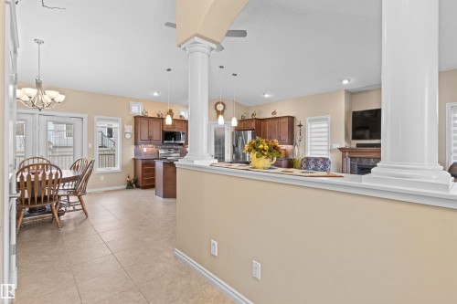Kitchen featuring decorative columns, decorative light fixtures, light tile patterned floors, stainless steel appliances, and brown cabinetry - 50 Willow Wood Lane, Stony Plain, AB - Indoor Photo Showing Kitchen With Upgraded Kitchen