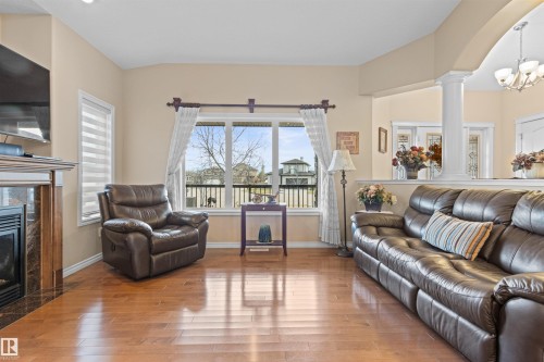 Living room featuring a premium fireplace, healthy amount of natural light, a chandelier, and wood finished floors - 50 Willow Wood Lane, Stony Plain, AB - Indoor Photo Showing Living Room With Fireplace