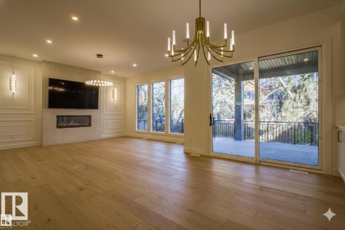 Unfurnished living room with a chandelier, light wood-type flooring, and a large fireplace - 12304 39 Avenue, Edmonton, AB 