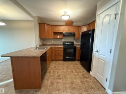 Kitchen with black appliances, brown cabinetry, a peninsula, a textured ceiling, and under cabinet range hood - 