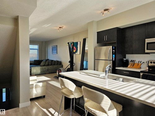 Kitchen featuring dark cabinetry, stainless steel appliances, light wood finished floors, a breakfast bar, and open floor plan - 83 600 Bellerose Drive, St. Albert, AB - Indoor Photo Showing Kitchen With Stainless Steel Kitchen With Double Sink