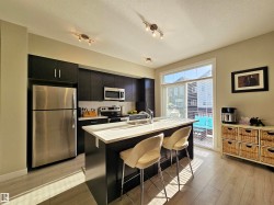 Kitchen featuring dark cabinetry, appliances with stainless steel finishes, light countertops, tasteful backsplash, and a center island with sink - 
