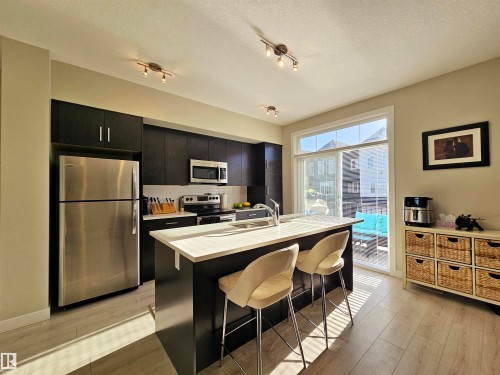 Kitchen featuring dark cabinetry, appliances with stainless steel finishes, light countertops, tasteful backsplash, and a center island with sink - 83 600 Bellerose Drive, St. Albert, AB - Indoor Photo Showing Kitchen With Stainless Steel Kitchen