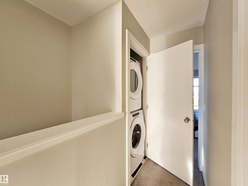 Laundry area with estacked washer and dryer, carpet flooring, and a textured ceiling - 83 600 Bellerose Drive, St. Albert, AB - Indoor Photo Showing Laundry Room