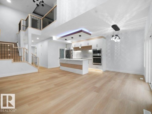Unfurnished living room with a towering ceiling, light wood-style floors, a chandelier, and stairs - 15419 20 Street, Edmonton, AB - Indoor Photo Showing Kitchen