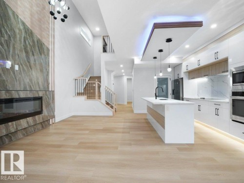 Kitchen featuring a fireplace, pendant lighting, light wood finished floors, white cabinetry, and recessed lighting - 15419 20 Street, Edmonton, AB - Indoor Photo Showing Kitchen With Upgraded Kitchen