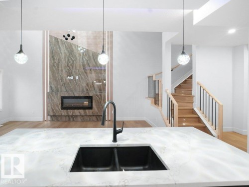 Kitchen with decorative light fixtures, light wood-style floors, light stone counters, and a high end fireplace - 15419 20 Street, Edmonton, AB - Indoor Photo Showing Kitchen
