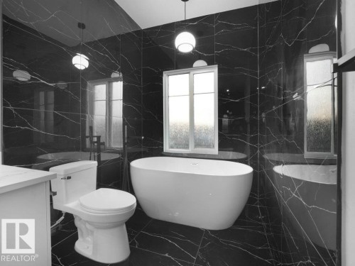 Full bath featuring tile walls, dark marble finish flooring, a freestanding bath, vanity, and stone wall - 15419 20 Street, Edmonton, AB - Indoor Photo Showing Bathroom