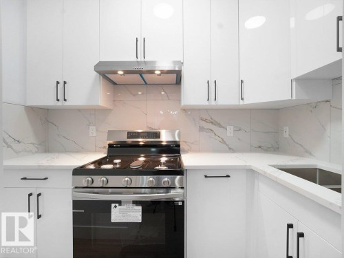 Kitchen with stainless steel range, white cabinetry, light stone counters, under cabinet range hood, and tasteful backsplash - 15419 20 Street, Edmonton, AB - Indoor Photo Showing Kitchen With Upgraded Kitchen