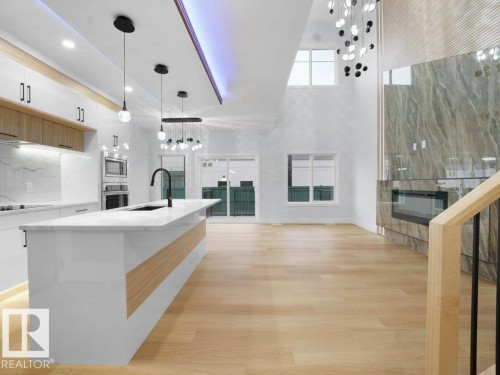 Kitchen featuring pendant lighting, light wood finished floors, a fireplace, a towering ceiling, and appliances with stainless steel finishes - 15419 20 Street, Edmonton, AB - Indoor Photo Showing Kitchen With Upgraded Kitchen