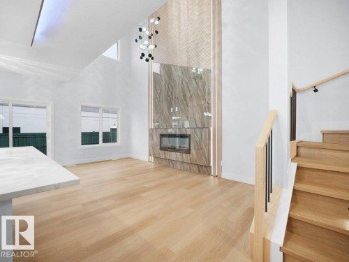Unfurnished living room with light wood finished floors, high vaulted ceiling, stairway, and a large fireplace - 15419 20 Street, Edmonton, AB - Indoor Photo Showing Other Room