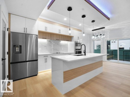 Kitchen with decorative light fixtures, stainless steel appliances, light wood-type flooring, light stone countertops, and a center island with sink - 15419 20 Street, Edmonton, AB - Indoor Photo Showing Kitchen With Stainless Steel Kitchen With Upgraded Kitchen