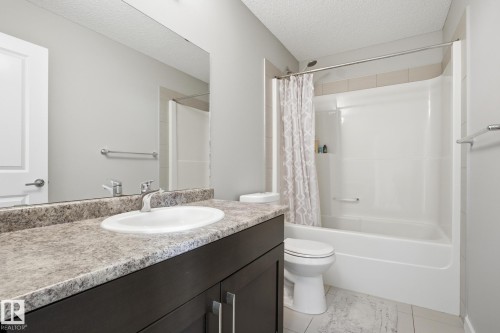 Full bath featuring a textured ceiling, vanity, light tile patterned floors, and shower / tub combo - 893 Ebbers Crescent Nw, Edmonton, AB - Indoor Photo Showing Bathroom