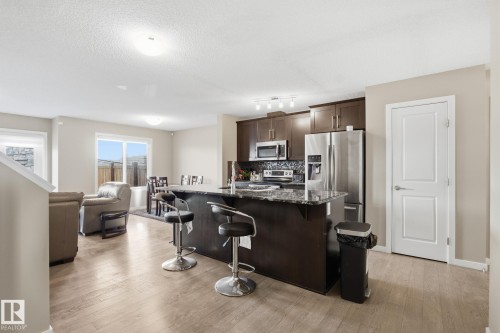 Kitchen with dark brown cabinetry, dark stone countertops, a breakfast bar area, stainless steel appliances, and a kitchen island with sink - 893 Ebbers Crescent Nw, Edmonton, AB - Indoor Photo Showing Kitchen With Upgraded Kitchen