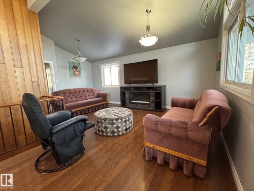 Living area featuring a glass covered fireplace, vaulted ceiling, and wood finished floors - 4707 53 Street, Athabasca Town, AB - Indoor Photo Showing Living Room