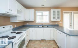 Kitchen featuring white appliances, dark countertops, a peninsula, white cabinetry, and under cabinet range hood - 