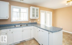 Kitchen featuring a peninsula, white cabinetry, dishwasher, glass insert cabinets, and dark countertops - 