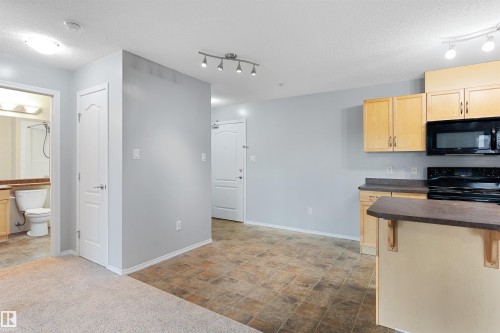 Kitchen with dark countertops, black appliances, a textured ceiling, light brown cabinets, and stone finish floors - 111 5951 165 Avenue, Edmonton, AB - Indoor Photo Showing Kitchen