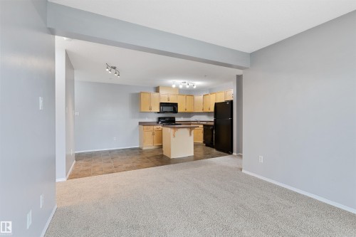 Kitchen with dark countertops, open floor plan, dark carpet, light brown cabinetry, and a kitchen breakfast bar - 111 5951 165 Avenue, Edmonton, AB - Indoor Photo Showing Kitchen