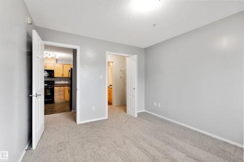 Unfurnished bedroom with light carpet, a textured ceiling, a spacious closet, and freestanding refrigerator - 111 5951 165 Avenue, Edmonton, AB - Indoor Photo Showing Other Room