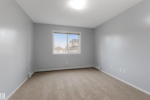 Spare room with light colored carpet, a textured ceiling, and a baseboard heating unit - 111 5951 165 Avenue, Edmonton, AB - Indoor Photo Showing Other Room
