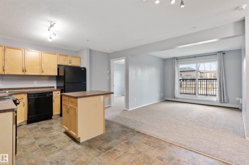 Kitchen featuring light brown cabinets, dark countertops, stone finish floors, black appliances, and a textured ceiling - 111 5951 165 Avenue, Edmonton, AB - Indoor Photo Showing Kitchen With Double Sink