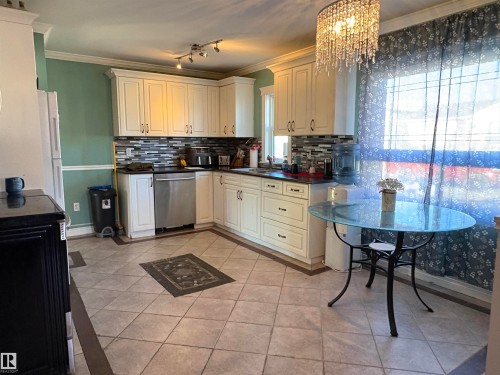 Kitchen with crown molding, dark countertops, light tile patterned floors, tasteful backsplash, and stainless steel dishwasher - 4813 52 Avenue, Elk Point, AB - Indoor