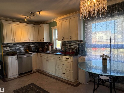 Kitchen featuring dark tile patterned flooring, dark countertops, decorative backsplash, inlaid floor details, and ornamental molding - 4813 52 Avenue, Elk Point, AB - Indoor Photo Showing Kitchen