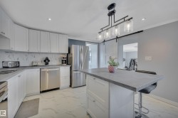 Kitchen with light marble finish flooring, a barn door, white cabinets, recessed lighting, and ornamental molding - 