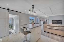 Kitchen with a kitchen bar, a barn door, white cabinetry, hanging light fixtures, and plenty of natural light - 