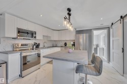 Kitchen with light marble finish flooring, appliances with stainless steel finishes, a breakfast bar, a barn door, and white cabinets - 