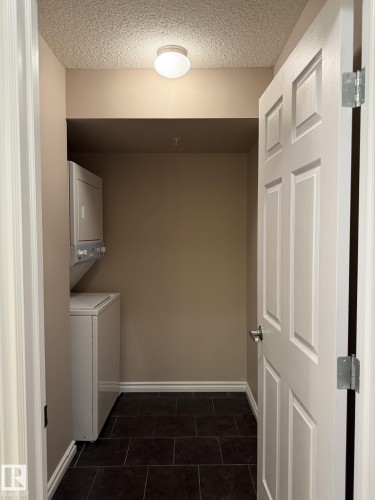 Washroom featuring stacked washer / drying machine, dark tile patterned floors, and a textured ceiling - 303 10118 106 Avenue, Edmonton, AB - Indoor